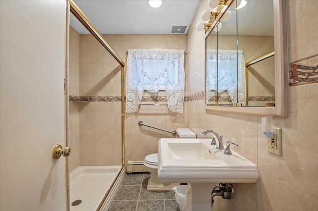 bathroom with tile patterned floors, a tile shower, baseboard heating, and tile walls