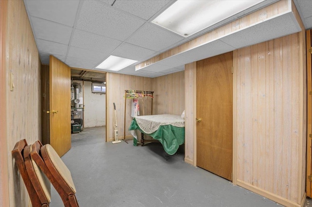 bedroom with a paneled ceiling, concrete flooring, and wooden walls