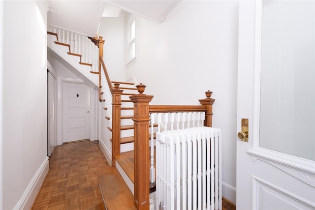 staircase with radiator heating unit, parquet floors, and crown molding