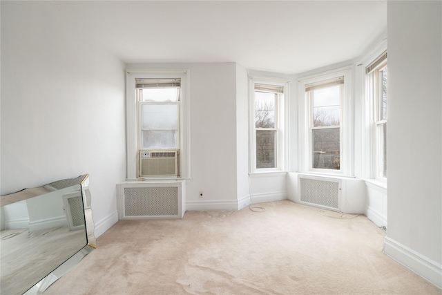 empty room featuring light carpet, radiator heating unit, and plenty of natural light