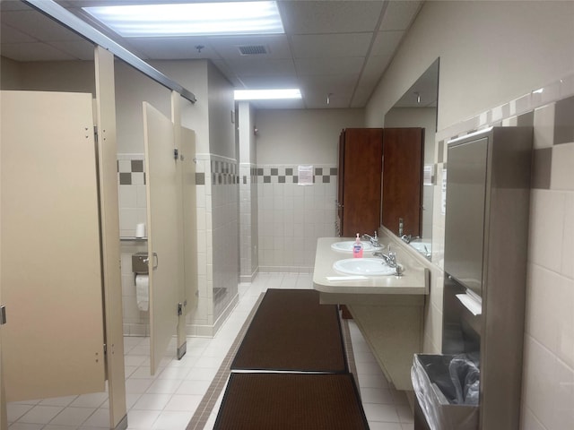 bathroom with visible vents, a drop ceiling, a sink, a shower stall, and tile walls