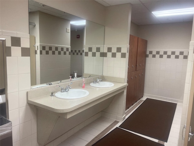 full bath featuring double vanity, a sink, and tile walls