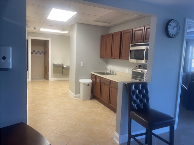 kitchen featuring light tile patterned floors, a drop ceiling, a sink, light countertops, and stainless steel microwave