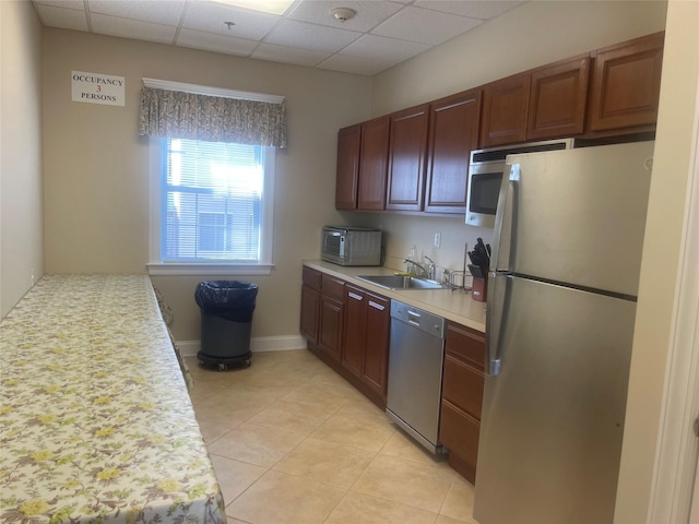 kitchen featuring light tile patterned floors, light countertops, appliances with stainless steel finishes, a sink, and a drop ceiling