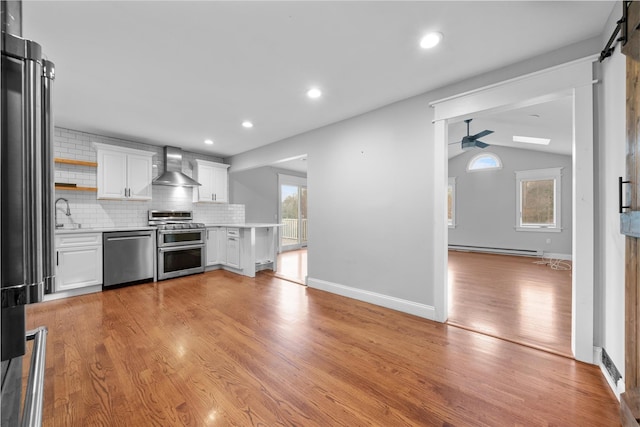 kitchen featuring white cabinets, wall chimney exhaust hood, appliances with stainless steel finishes, and light hardwood / wood-style flooring