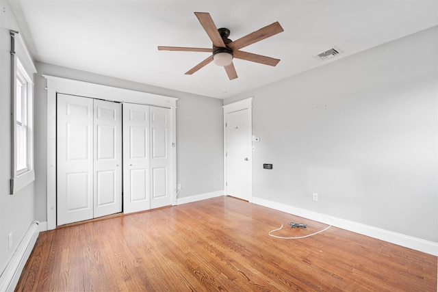 unfurnished bedroom featuring multiple windows, ceiling fan, a baseboard radiator, and wood-type flooring