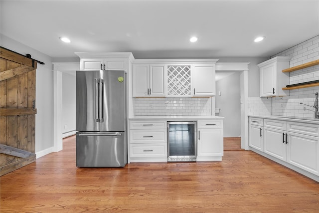 kitchen with stainless steel fridge, beverage cooler, a barn door, light hardwood / wood-style flooring, and white cabinetry