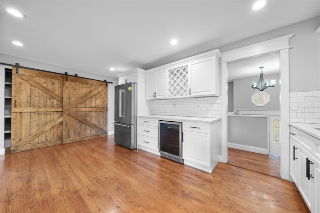 kitchen with beverage cooler, a barn door, light hardwood / wood-style flooring, white cabinetry, and stainless steel refrigerator