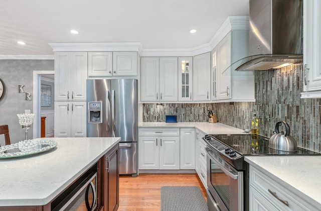 kitchen featuring white cabinetry, appliances with stainless steel finishes, wall chimney exhaust hood, and crown molding