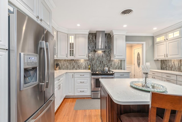 kitchen featuring stainless steel appliances, white cabinetry, a center island, and wall chimney range hood