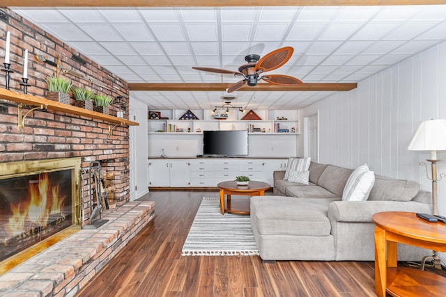 living room featuring built in shelves, dark hardwood / wood-style floors, a fireplace, and ceiling fan