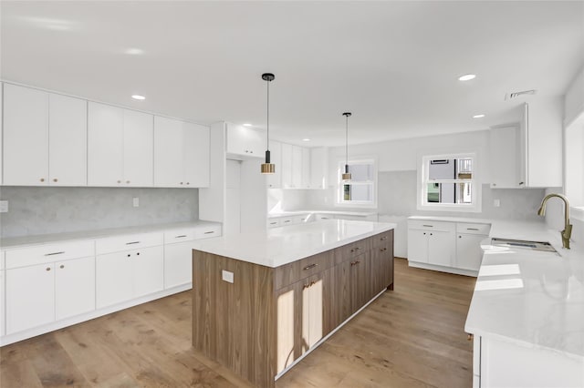 kitchen with white cabinets, light hardwood / wood-style floors, a kitchen island, and sink