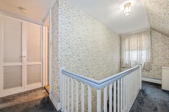 hallway featuring lofted ceiling and dark colored carpet