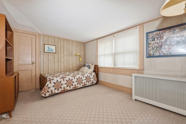 bedroom with radiator heating unit, light carpet, and wooden walls