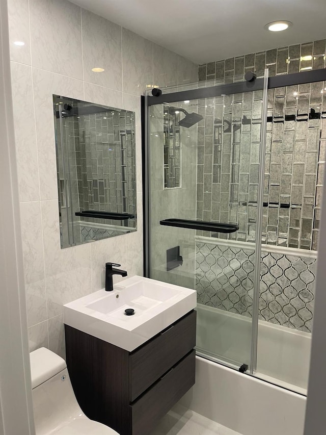 full bathroom with shower / bath combination with glass door, vanity, toilet, and tile walls