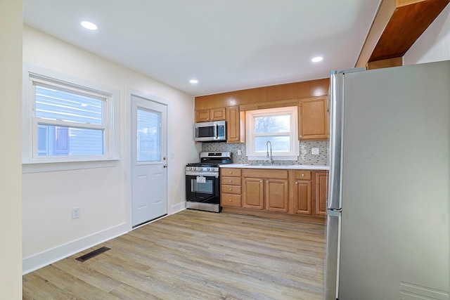 kitchen with tasteful backsplash, sink, light hardwood / wood-style floors, and appliances with stainless steel finishes