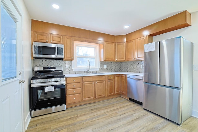 kitchen with appliances with stainless steel finishes, light wood-type flooring, tasteful backsplash, and sink