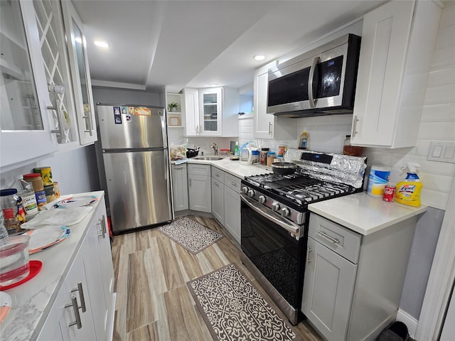 kitchen featuring appliances with stainless steel finishes, backsplash, light stone counters, sink, and light hardwood / wood-style flooring