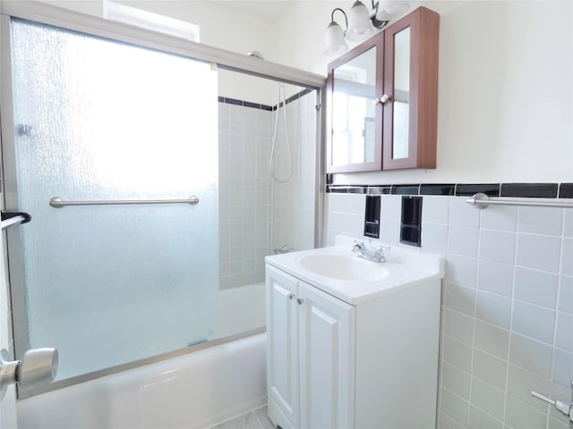 bathroom with combined bath / shower with glass door, vanity, plenty of natural light, and tile walls