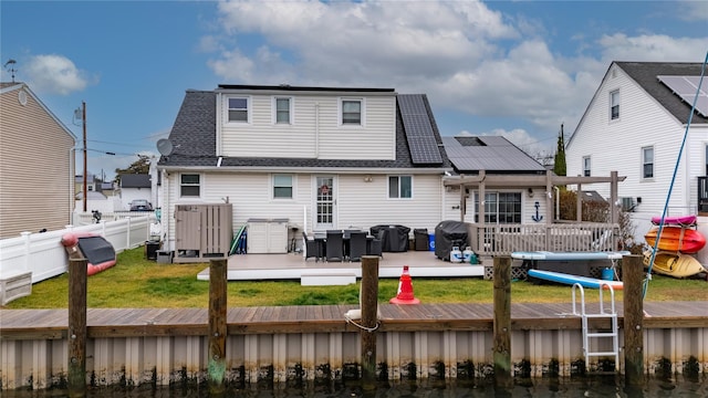 back of property with a lawn, solar panels, and a deck with water view