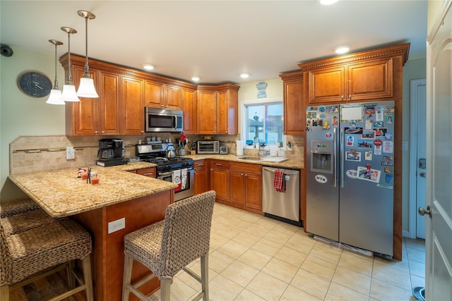 kitchen featuring light stone counters, kitchen peninsula, pendant lighting, a kitchen bar, and appliances with stainless steel finishes