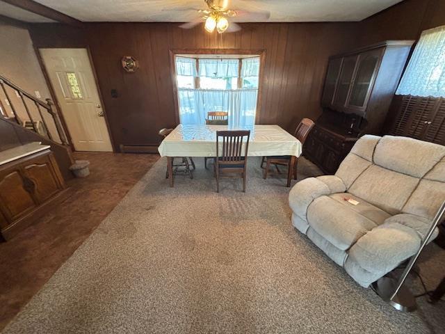 dining room with ceiling fan, a baseboard radiator, dark carpet, and wood walls