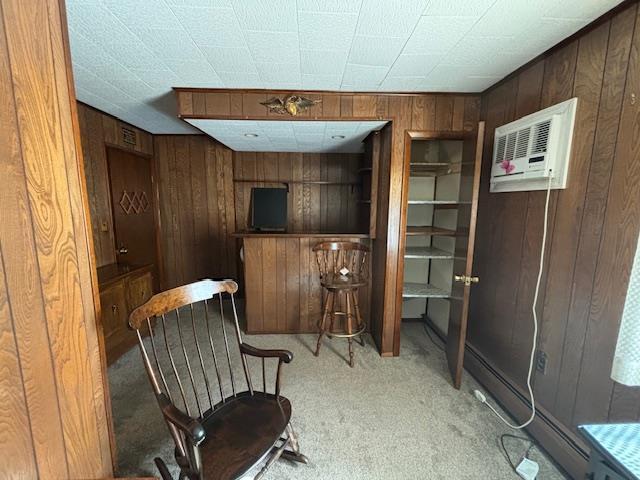 sitting room with a wall mounted AC, wood walls, and light colored carpet