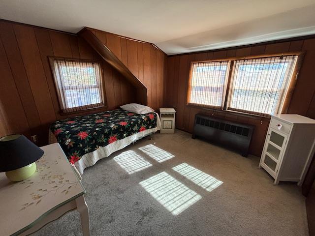 bedroom with light colored carpet, radiator heating unit, wooden walls, and vaulted ceiling