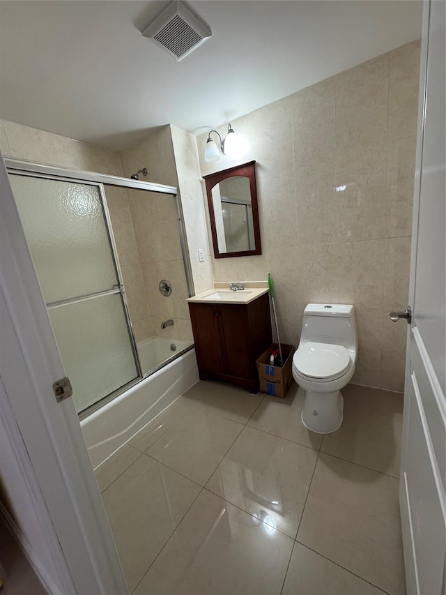 full bathroom with tile patterned flooring, toilet, shower / bath combination with glass door, vanity, and tile walls