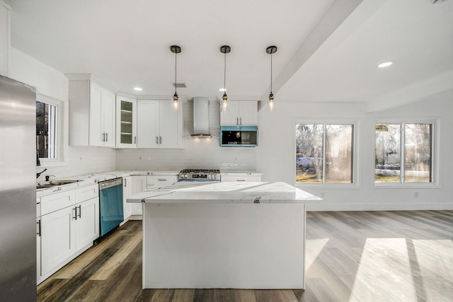 kitchen with a center island, wall chimney range hood, hardwood / wood-style flooring, white cabinetry, and stainless steel appliances