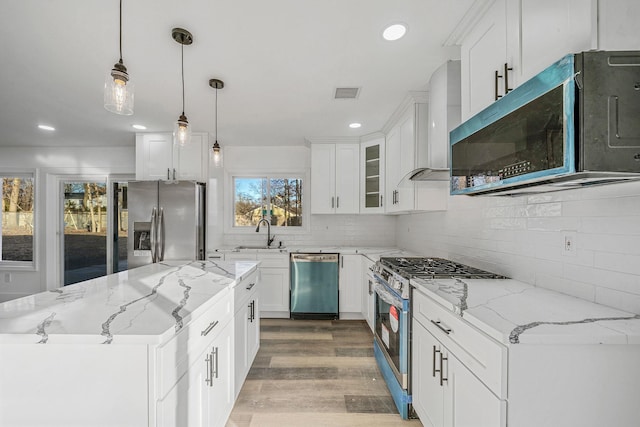 kitchen featuring white cabinets, light hardwood / wood-style flooring, light stone countertops, appliances with stainless steel finishes, and decorative light fixtures