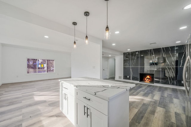 kitchen with pendant lighting, light stone countertops, a fireplace, light wood-type flooring, and white cabinetry