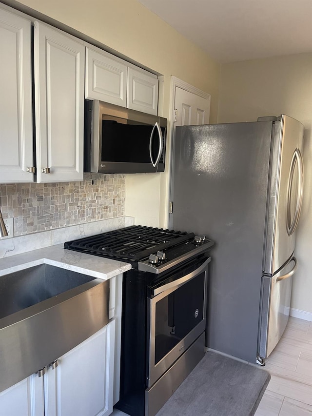 kitchen with sink, decorative backsplash, light wood-type flooring, appliances with stainless steel finishes, and white cabinetry