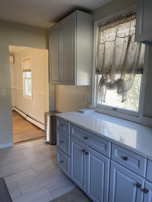 kitchen with light stone countertops, light wood-type flooring, baseboard heating, and a wealth of natural light