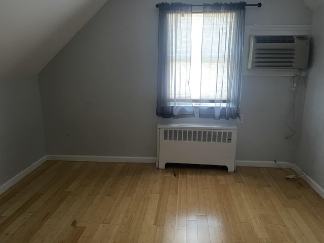 additional living space with an AC wall unit, lofted ceiling, radiator, and light hardwood / wood-style flooring