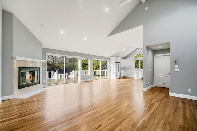 unfurnished living room with a tiled fireplace, high vaulted ceiling, and light hardwood / wood-style floors