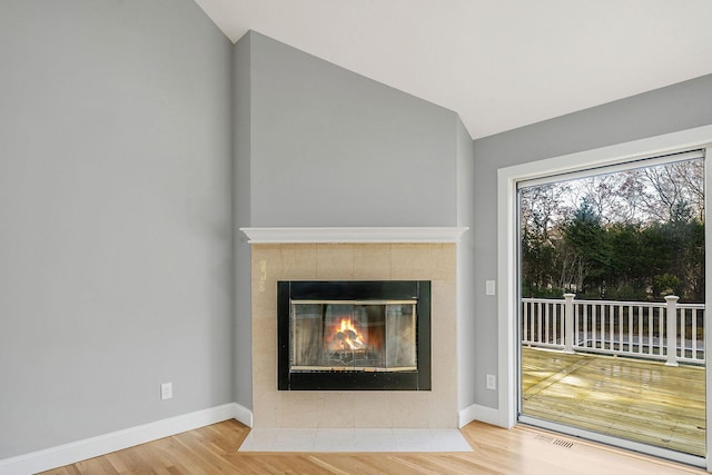 unfurnished living room with a tile fireplace, hardwood / wood-style floors, and lofted ceiling