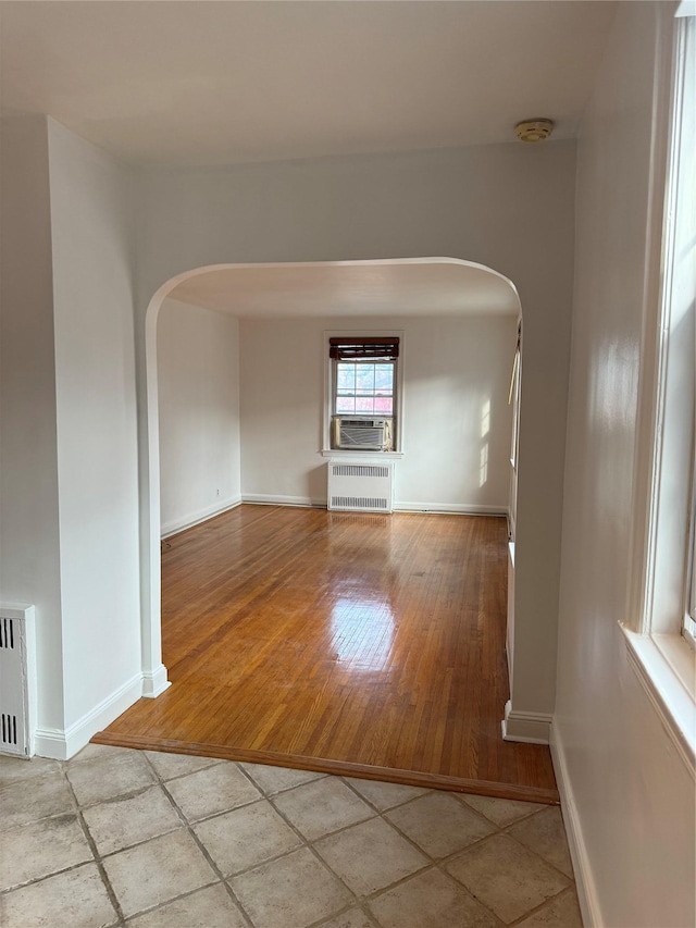 unfurnished room featuring cooling unit, light wood-type flooring, and radiator heating unit