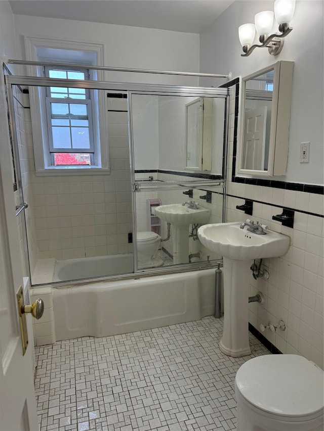 bathroom with tile patterned flooring, combined bath / shower with glass door, a notable chandelier, toilet, and tile walls