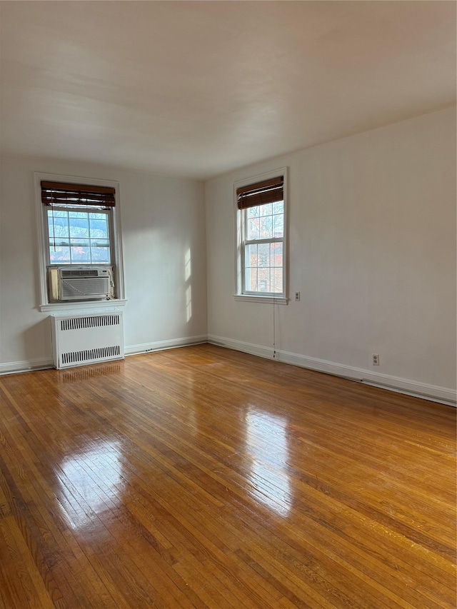 empty room featuring hardwood / wood-style floors, plenty of natural light, cooling unit, and radiator heating unit