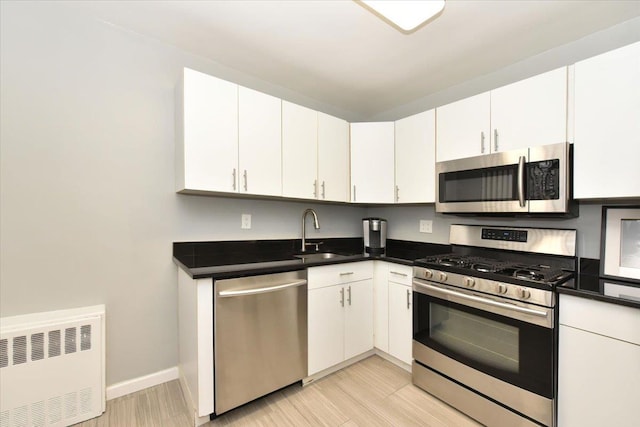 kitchen featuring appliances with stainless steel finishes, radiator heating unit, white cabinetry, and sink