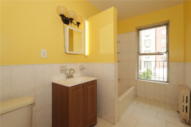 bathroom featuring radiator, vanity, tile walls, toilet, and a bathing tub