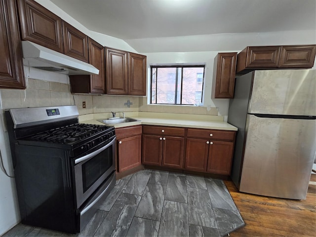 kitchen with light countertops, a sink, under cabinet range hood, stainless steel appliances, and decorative backsplash