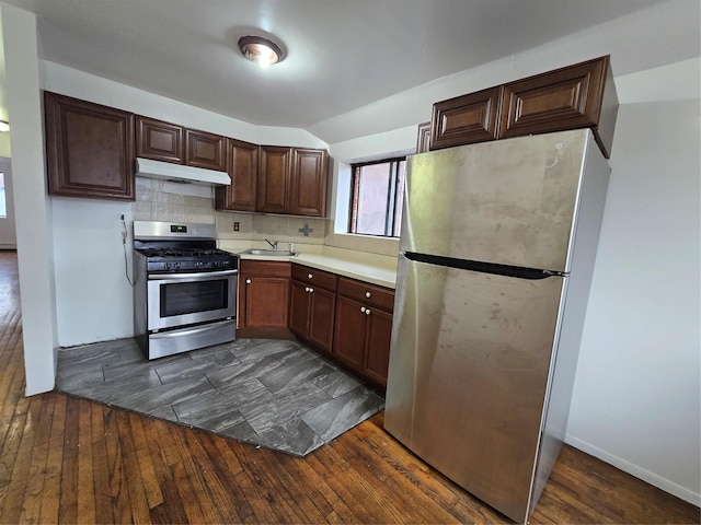 kitchen featuring decorative backsplash, stainless steel appliances, under cabinet range hood, a sink, and dark wood-style floors