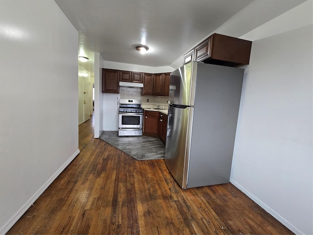 kitchen featuring light countertops, stainless steel appliances, dark wood-type flooring, under cabinet range hood, and backsplash