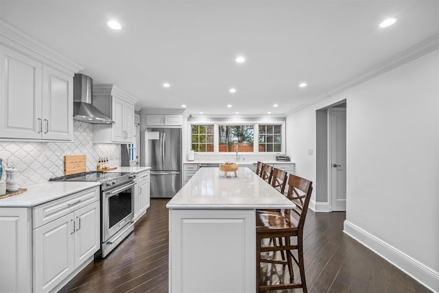 kitchen with white cabinetry, dark wood-type flooring, stainless steel appliances, wall chimney range hood, and a kitchen island