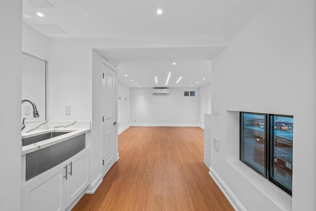 bar with a wall mounted AC, sink, white cabinets, and light wood-type flooring