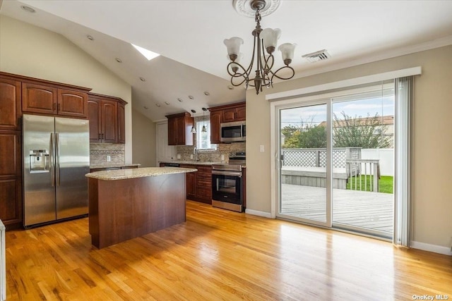 kitchen with appliances with stainless steel finishes, a center island, decorative light fixtures, tasteful backsplash, and vaulted ceiling