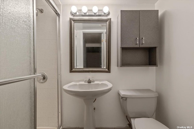 bathroom featuring toilet, a shower with shower door, and sink