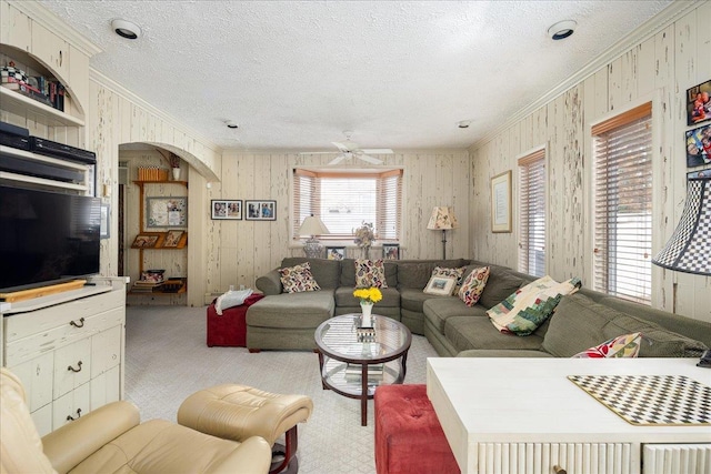 carpeted living room with a textured ceiling, ceiling fan, crown molding, and wood walls